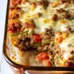 Ground Beef Zucchini Casserole | Easy Low-Carb Dinner Idea 9 Cheesy baked ground beef zucchini casserole in a glass dish with golden bubbly top and visible tomato layers.