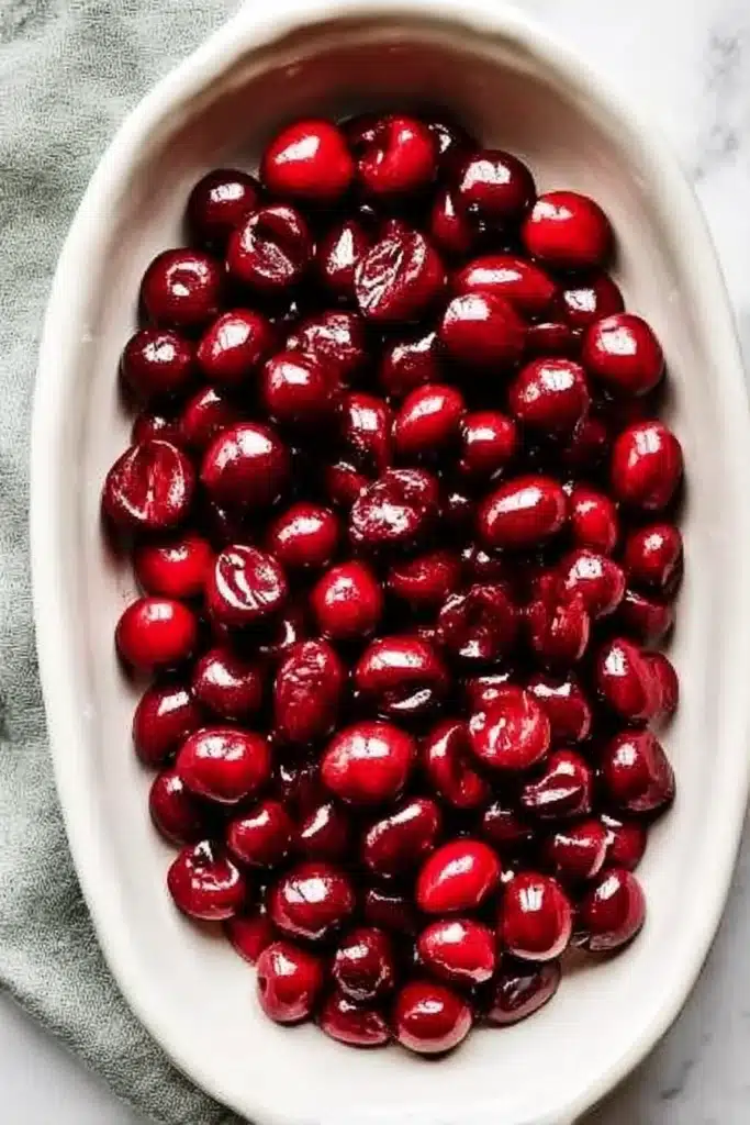 Fresh pitted cherries in an oval cream ceramic baking dish, ready for baking.

