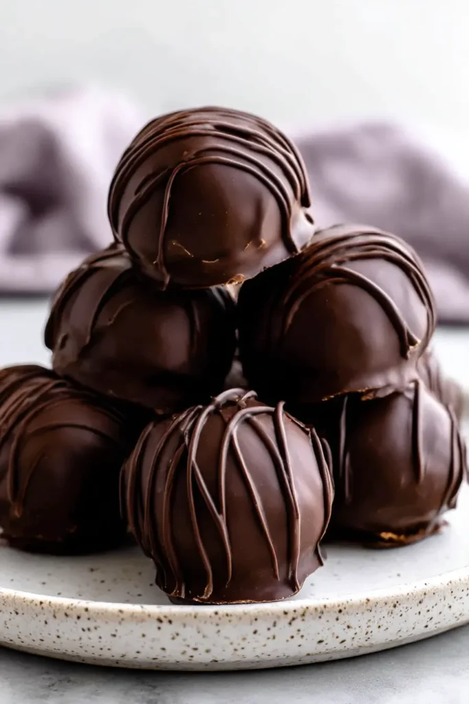 Stack of no-bake chocolate peanut butter balls with glossy drizzle on ceramic plate.