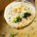 Ladle filled with creamy broccoli cheddar soup, showcasing melted cheese and fresh broccoli in a thick, rich base.