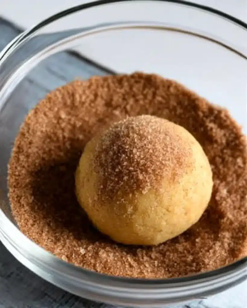 Pumpkin snickerdoodle dough ball rolled in cinnamon sugar in glass bowl

