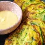 4-Ingredient Zucchini Fritters: Quick, Crispy & Absolutely Delicious 9 Close-up of crispy 4-ingredient zucchini fritters with golden edges and shredded zucchini, served with creamy dipping sauce in a pink ceramic bowl.