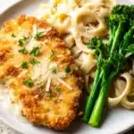 Parmesan Crusted Chicken – Crispy, Juicy, and Ready Fast 9 Golden parmesan crusted chicken with creamy fettuccine alfredo and steamed broccolini on a white plate
