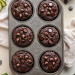 Chocolate Zucchini Muffins Delicious & Easy 11 Moist chocolate zucchini muffins with chocolate chips in a rustic muffin pan, styled with zucchini ribbons and cocoa powder on a cozy kitchen backdrop.