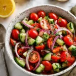Cucumber Tomato Salad – Delicious & Zesty Summer Classic 7 Fresh cucumber tomato salad in a white ceramic bowl with red onions, grape tomatoes, parsley, and lemon on a stone background