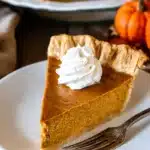 Easy Pumpkin Pie Recipe – Absolutely Delicious & Foolproof 9 Easy Pumpkin Pie Recipe slice on a white plate with whipped cream and flaky golden crust, served on a rustic table