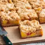 Peaches and Cream Crumble Bars – Buttery, Fruity, and Easy to Bake 6 Golden peaches and cream crumble bars with a crisp buttery topping, served on a rustic board over a wooden table.