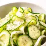 Cucumber Vinegar Salad – Simple, Tangy & Refreshing Favorite 9 Thinly sliced cucumber vinegar salad with onions and dill in a white bowl, garnished with black pepper.