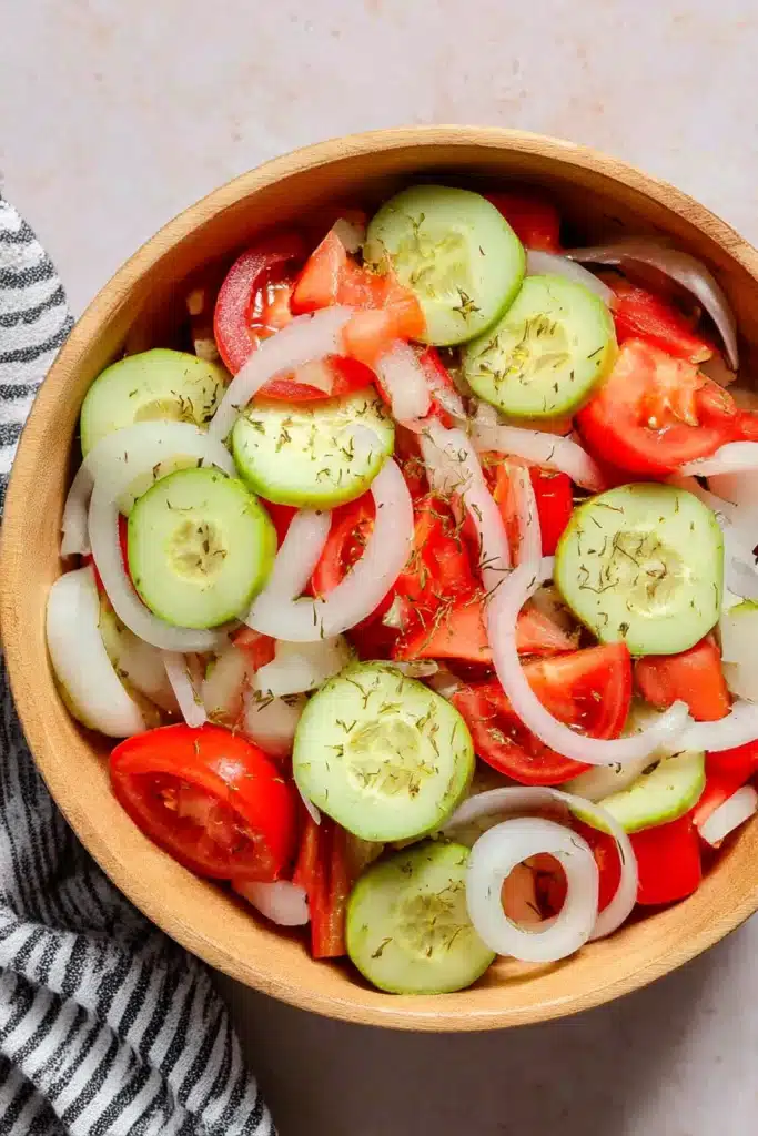 Top view of marinated cucumber, tomato, and onion salad in a wooden bowl on a rustic table