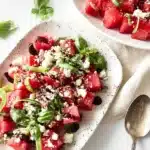Fresh Watermelon Feta Salad – Light, Juicy, and Summer-Perfect 12 Fresh watermelon feta salad with basil, balsamic glaze, and feta crumbles on a ceramic plate, styled with leafy greens and vintage cutlery.