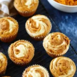 Pumpkin cream cheese muffins with creamy swirled tops on a cooling rack beside a bowl of pumpkin purée.