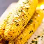 Garlic Parmesan Grilled Corn on the Cob stacked on a rustic plate with melted butter and parsley