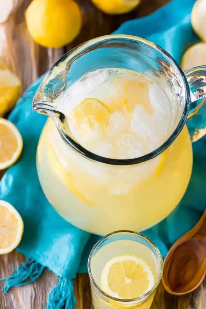 Glass pitcher of chilled homemade lemonade with ice and lemon slices on rustic wooden table

