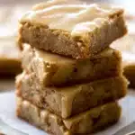 Maple Glazed Apple Blondies – Easy Fall Dessert Recipe 6 Chewy maple glazed apple blondies stacked on a plate, topped with a glossy maple icing and filled with chunks of baked apple.