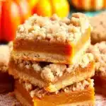 Pumpkin Pie Bars – Stunningly Easy & Delicious Fall Treat 9 Pumpkin pie bars with crumb topping and creamy filling stacked on a plate with fall pumpkins in the background.