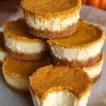 Mini Pumpkin Cheesecakes: Creamy Fall Dessert Bites 6 Mini pumpkin cheesecakes stacked on a ceramic plate, showing creamy cheesecake and spiced pumpkin layers with a graham cracker crust