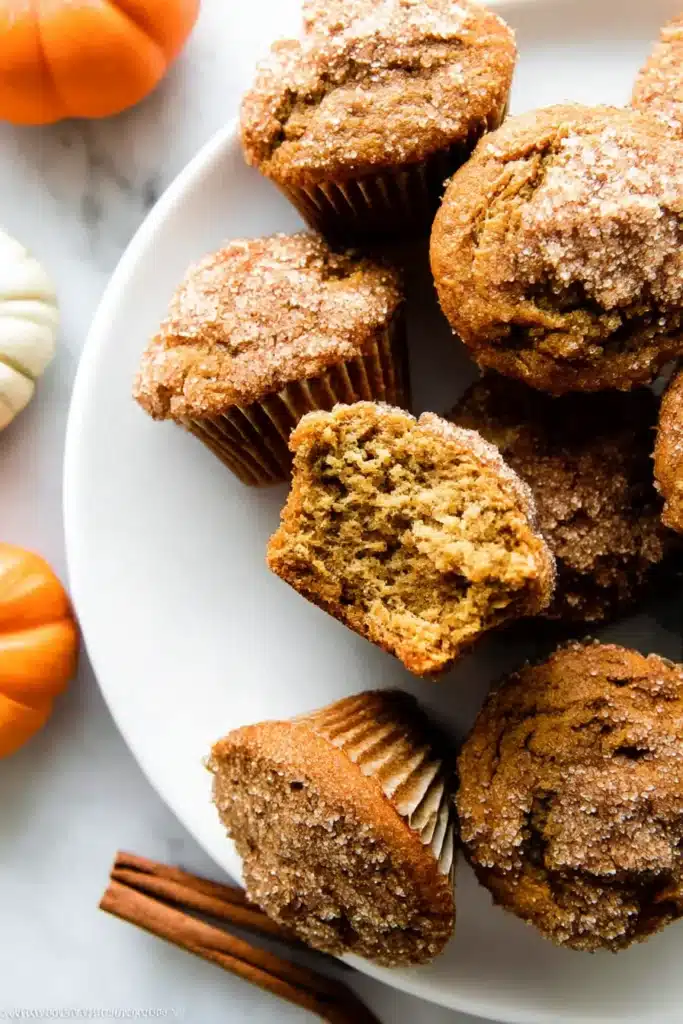 Easy Pumpkin Muffins – Super Moist One-Bowl Fall Recipe 11 Close-up of pumpkin muffins on a plate, with one broken open to show soft, moist crumb and sugar topping