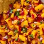 Fresh peach mango salsa with diced fruit, peppers, onion, and cilantro served with a tortilla chip in a ceramic bowl