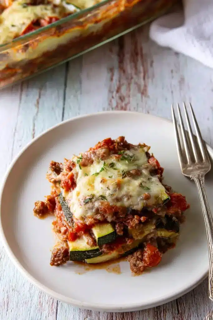 Single serving of ground beef zucchini casserole topped with melted cheese on a white plate

