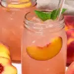 Homemade peach lemonade in mason jars with peach slices, mint, and ice, served with fresh peaches