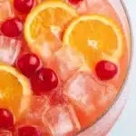 Shirley Temple Party Punch – Easy, Fizzy & Fun Summer Drink 9 Close-up of Shirley Temple party punch with ice cubes, orange slices, and maraschino cherries in a glass bowl.