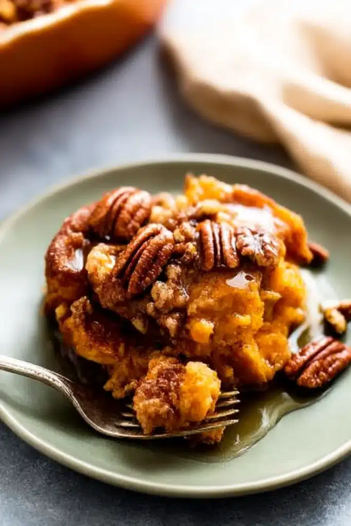 Slice of pumpkin French toast casserole with pecan topping and maple syrup on a green plate.

