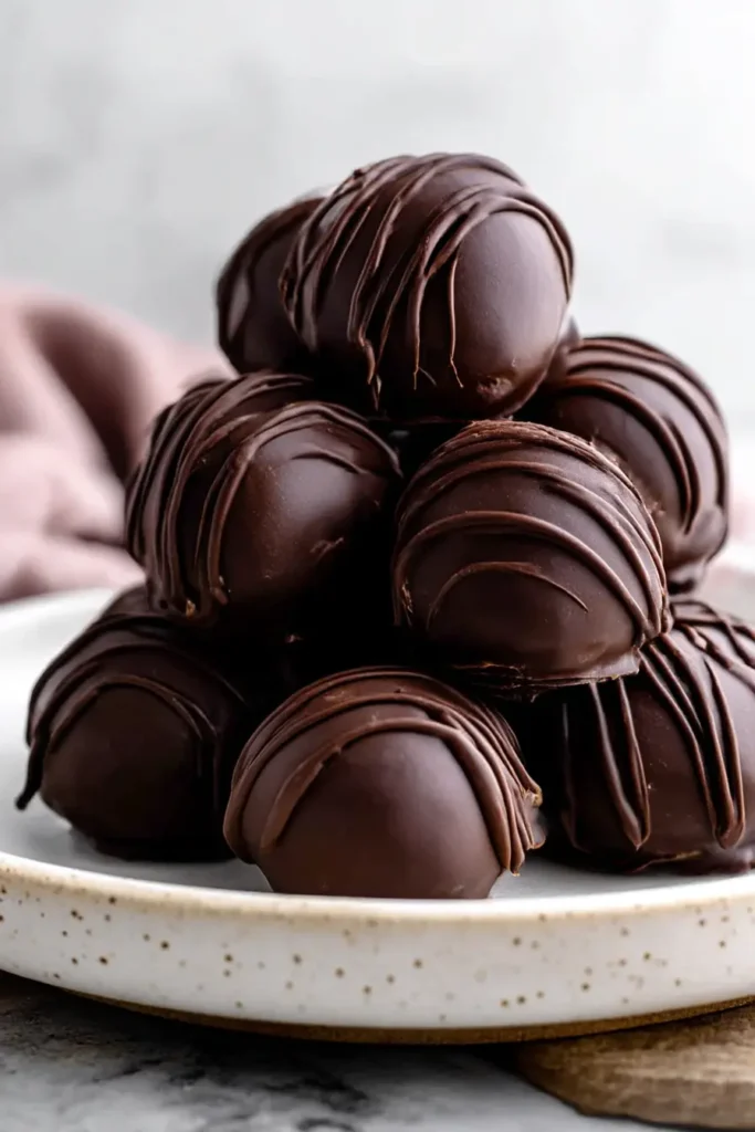 Stacked chocolate peanut butter balls with smooth coating and chocolate drizzle on a ceramic plate

