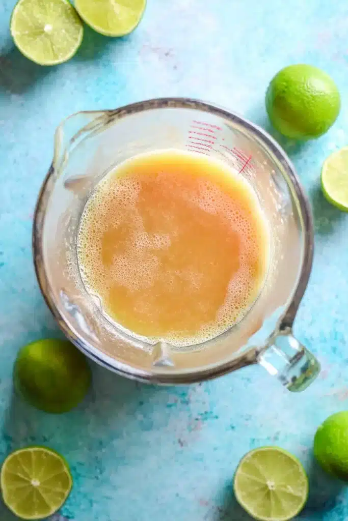 Pineapple Peach Agua Fresca: Easy, Refreshing Summer Drink 10 Blended pineapple peach juice in a glass measuring cup with fresh limes on a rustic teal surface