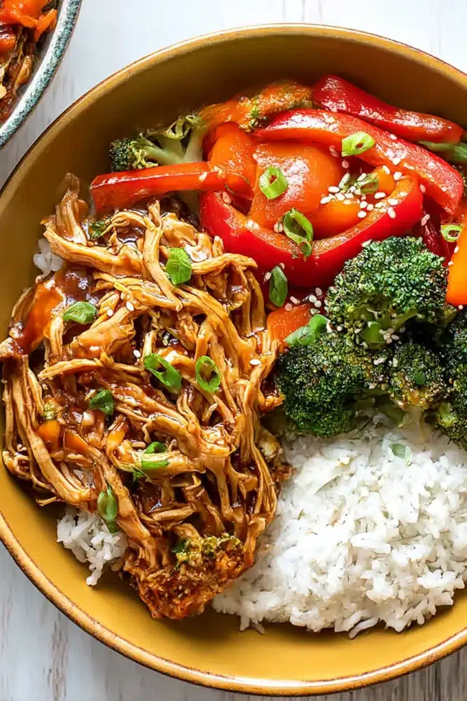 Teriyaki chicken bowl with stir-fried vegetables and rice topped with sesame seeds and green onions

