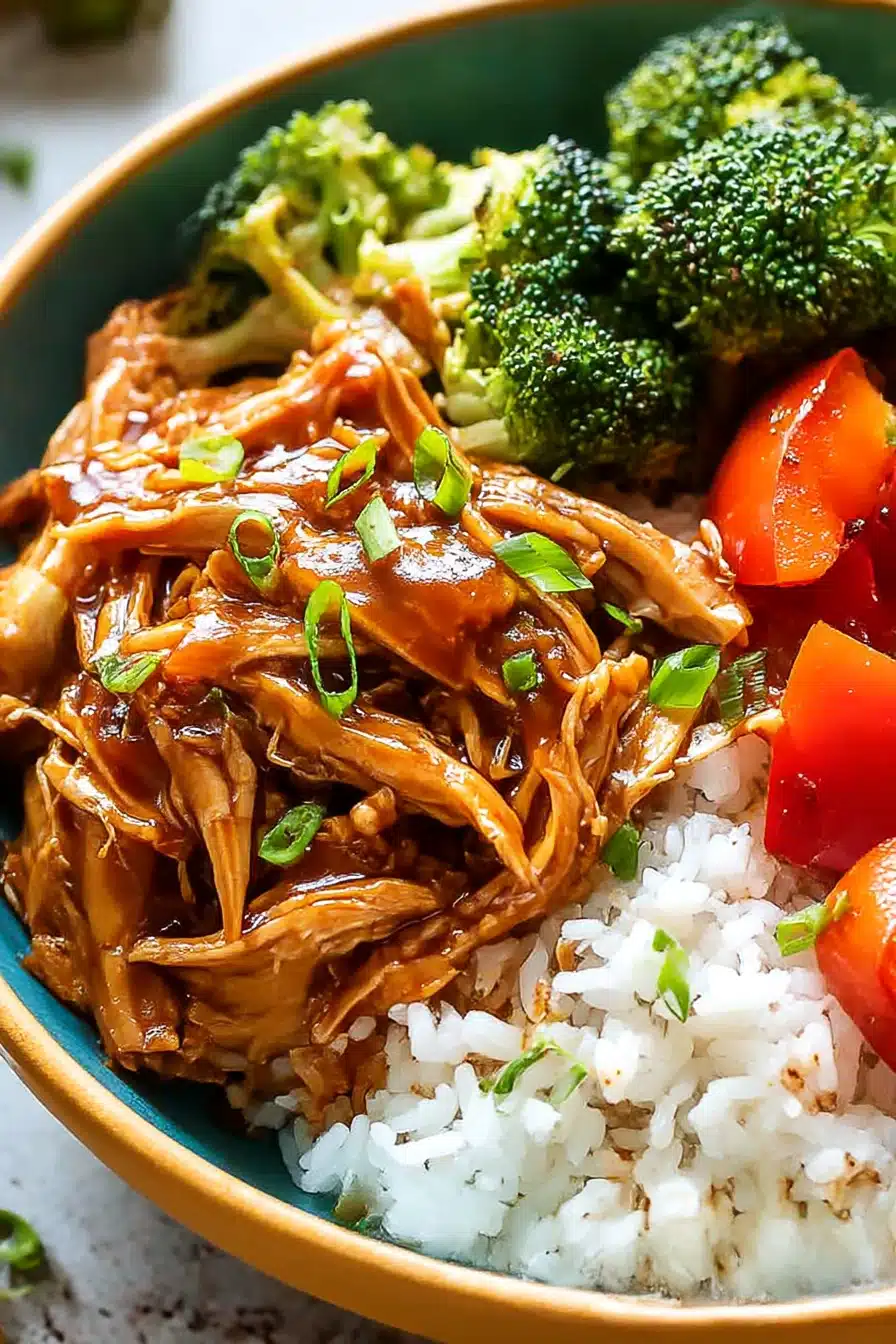 Shredded teriyaki chicken with vegetables and rice in a ceramic bowl topped with green onions