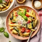 Tomato Zucchini Pasta – Quick, Fresh & Easy Recipe 9 A bowl of tomato zucchini pasta with penne, blistered cherry tomatoes, sautéed zucchini, fresh basil, and grated Parmesan cheese on a ceramic plate.