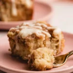 Banana Crumb Cake – The Perfect Coffee Cake 7 Moist banana crumb cake slice with cinnamon topping and cream cheese drizzle on a pink plate, fork holding a bite.