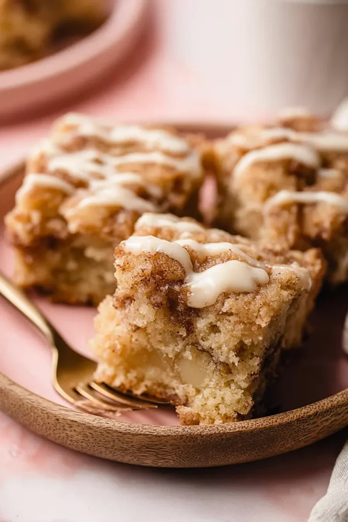 Banana Crumb Cake – The Perfect Coffee Cake 6 Top view of banana crumb cake squares with crumb topping and cream cheese drizzle in wooden tray, rustic napkin and coffee.