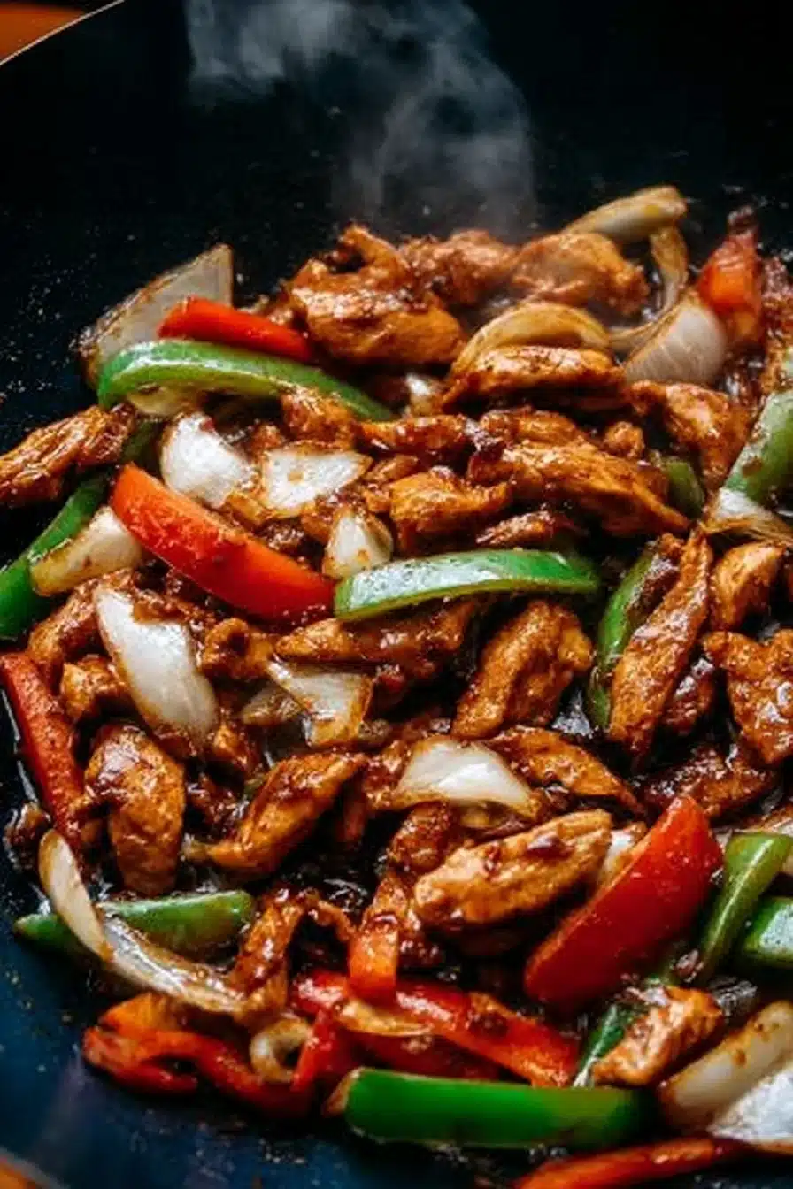 Black pepper chicken stir-fry with colorful bell peppers and onions in a glossy wok