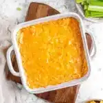 Buffalo Chicken Dip Recipe (Easy, Creamy & Crowd-Pleasing) 11 Buffalo chicken dip in white baking dish surrounded by celery sticks, carrots, and Frito Scoops on wood board