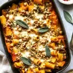 Cheesy pumpkin pasta bake topped with melted cheese, toasted walnuts, and sage in a cast iron dish