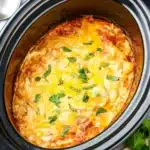 Slow Cooker Chicken Enchilada Casserole – Easy & Delicious 12 Slow Cooker Chicken Enchilada Casserole topped with melted cheese and herbs inside a black crockpot