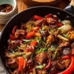 Chili Crisp Chicken – Quick, Flavorful & Easy Stir-Fry 6 Close-up of chili crisp chicken stir-fry with red peppers, onions, and scallions in a skillet, served with rice and chili oil.