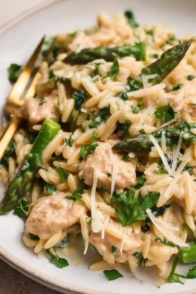 Close-up of creamy chicken orzo with asparagus, parmesan, and parsley on a white plate