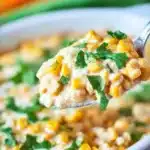 Spoonful of creamy Mexican Street Corn Casserole in a white ceramic bowl topped with fresh cilantro