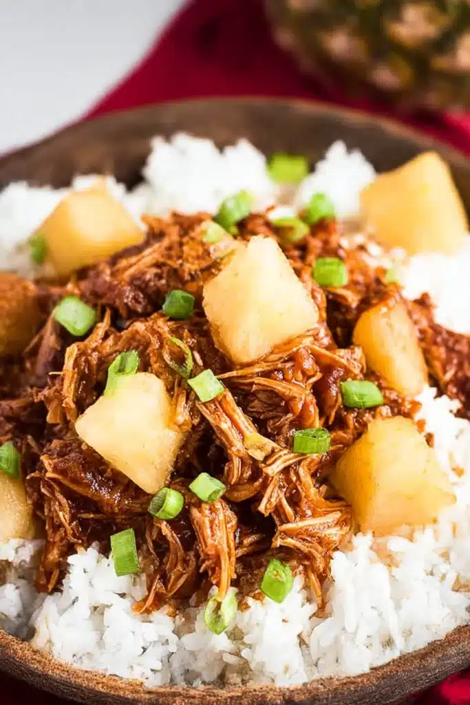 Shredded Crockpot Hawaiian BBQ Chicken with pineapple chunks over white rice in a charcoal bowl