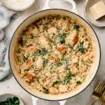 Creamy one pot chicken orzo with spinach and parmesan served in a white Dutch oven, styled with herbs and cheese on a light concrete background