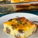 Easy sausage and egg casserole slice served on a white plate, topped with melted cheese and chives