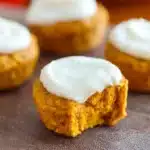 Flourless Pumpkin Muffins 7 Close-up of flourless pumpkin muffin topped with creamy white frosting on a rustic surface.