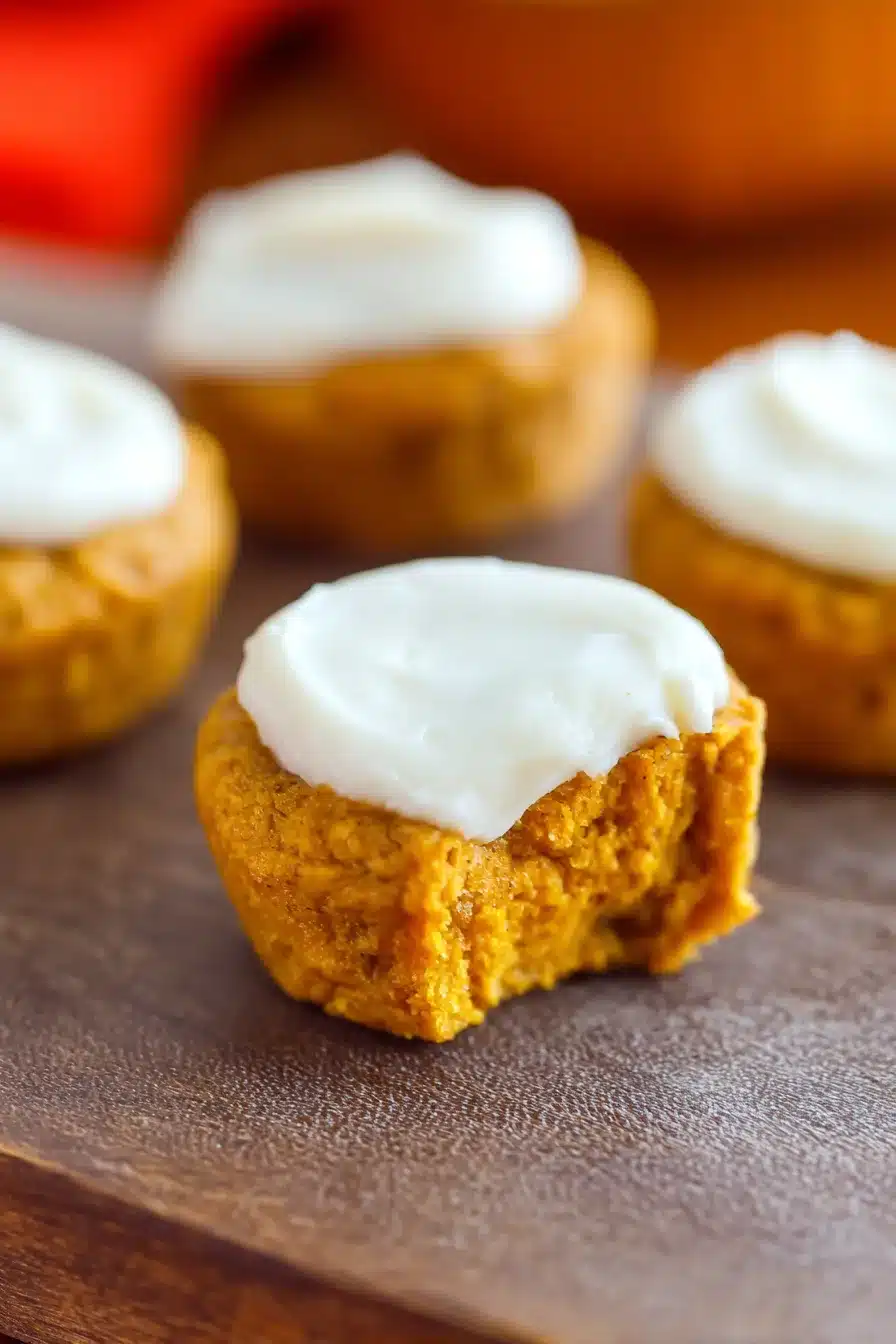 Close-up of flourless pumpkin muffin topped with creamy white frosting on a rustic surface.