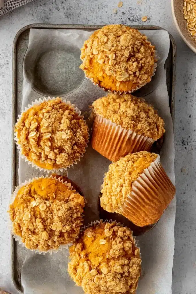 Pumpkin oatmeal muffins with crisp oat streusel in a parchment-lined tray on a light surface