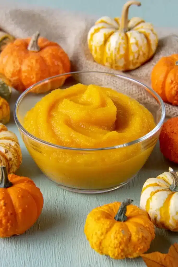 Glass bowl of smooth homemade pumpkin purée with assorted mini pumpkins