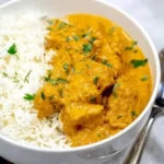 Creamy coconut chicken curry served with basmati rice in a white bowl, garnished with cilantro.