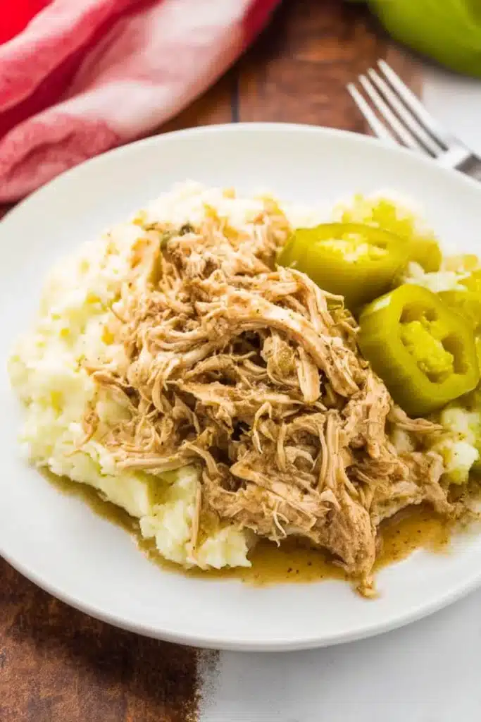 Shredded Mississippi chicken with mashed potatoes and pepperoncini served on a white plate