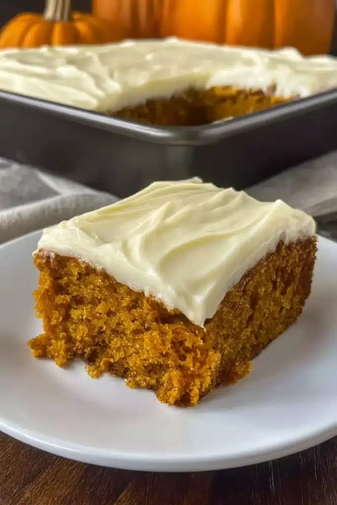 Slice of moist pumpkin carrot cake with cream cheese frosting on plate with tray in background
